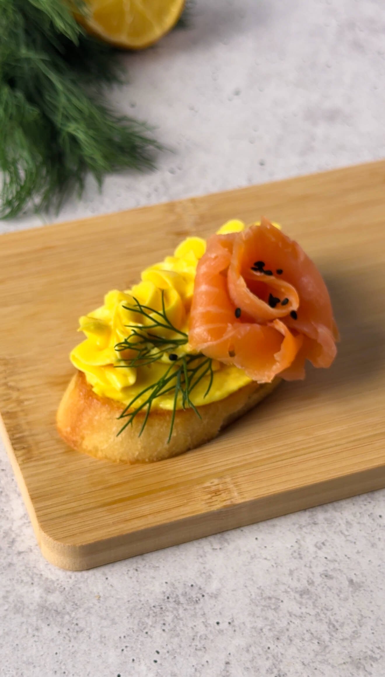 Close-up of one smoked salmon crostini with a salmon rose, golden mousse swirl, fresh dill, and crispy garlic-rubbed toast.