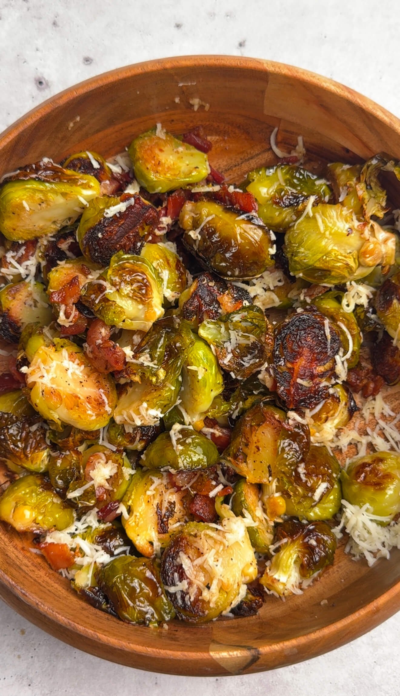 Roasted Brussels sprouts with bacon tossed with freshly grated Parmesan cheese in a wooden bowl