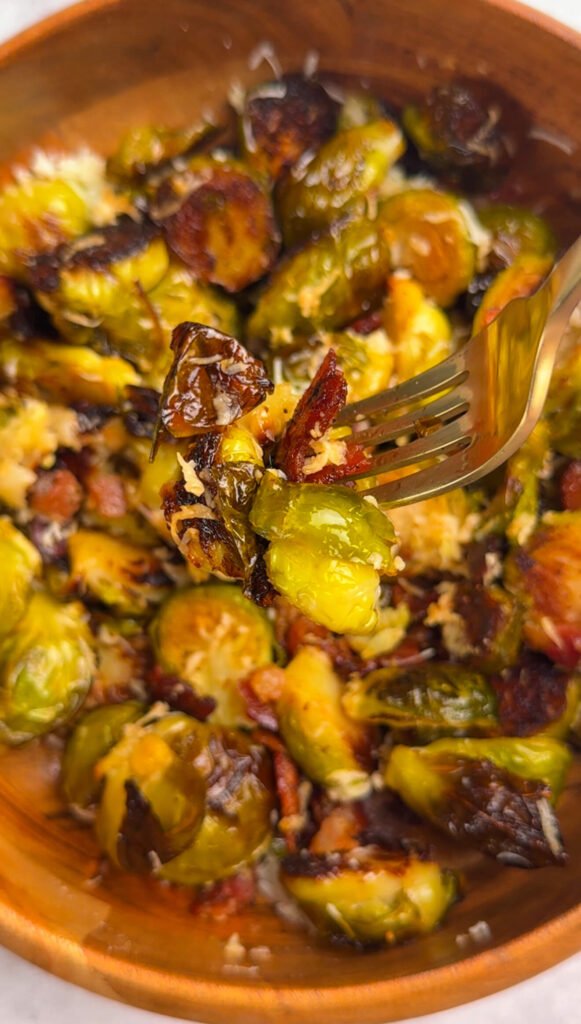 Close-up of a fork lifting crispy Brussels sprouts with melted Parmesan and bacon from a bowl
