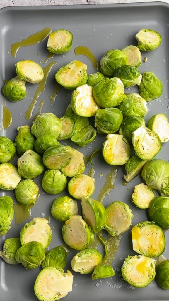 Halved Brussels sprouts drizzled with olive oil and sprinkled with salt on a baking sheet, ready to roast