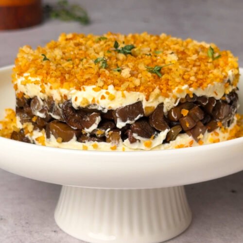 Layered Roasted Mushroom & Truffle Goat Cheese Timbale topped with golden garlic crumbs and fresh thyme, served on a white cake stand