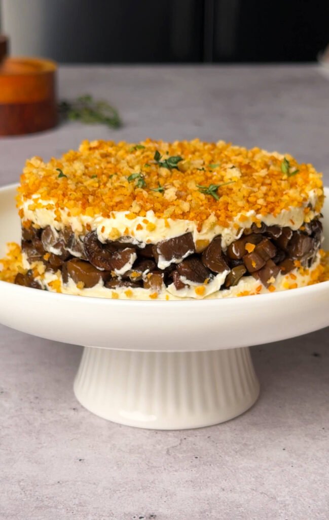 Layered mushroom truffle appetizer topped with golden garlic crumbs and fresh thyme, served on a white cake stand