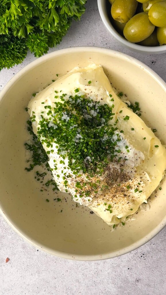 Cream cheese, sour cream, chives, salt, and pepper in a mixing bowl before being whipped together.