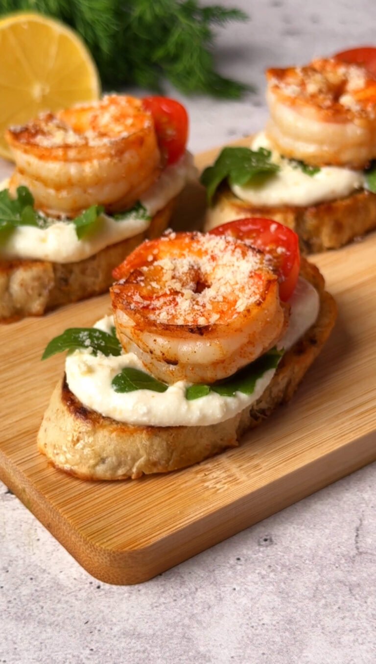 Finished shrimp crostini topped with seared shrimp, arugula, ricotta, cherry tomato, and grated Parmesan.