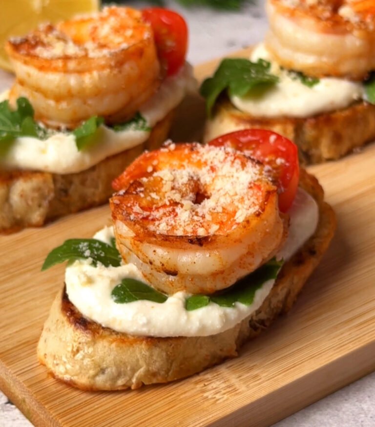 Finished shrimp crostini topped with seared shrimp, arugula, ricotta, cherry tomato, and grated Parmesan.