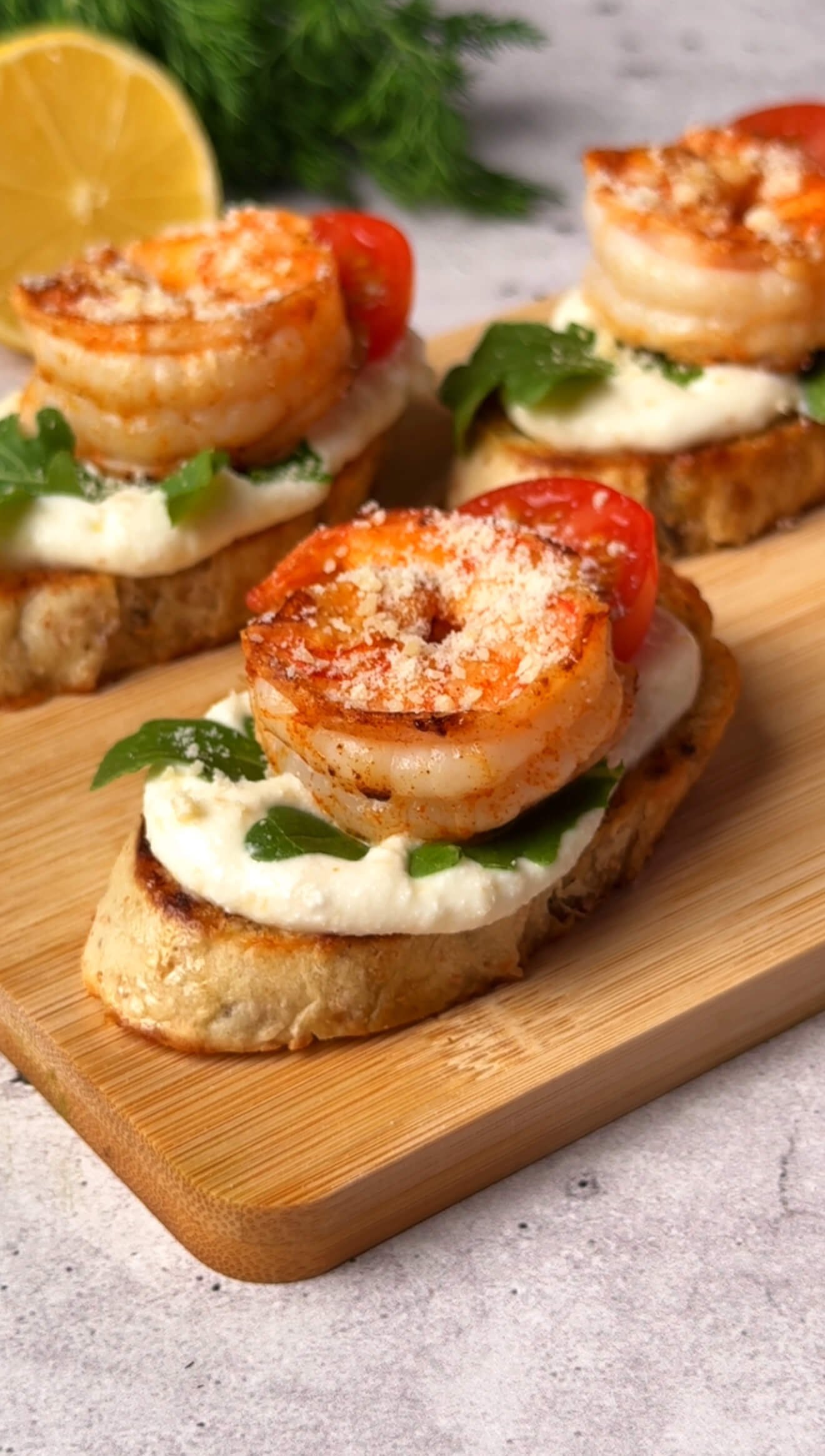 Finished shrimp crostini topped with seared shrimp, arugula, ricotta, cherry tomato, and grated Parmesan.