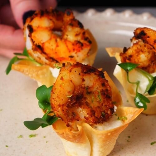 Crispy shrimp wonton cup filled with lime sour cream and topped with Cajun-spiced shrimp and microgreens, served as an elegant appetizer