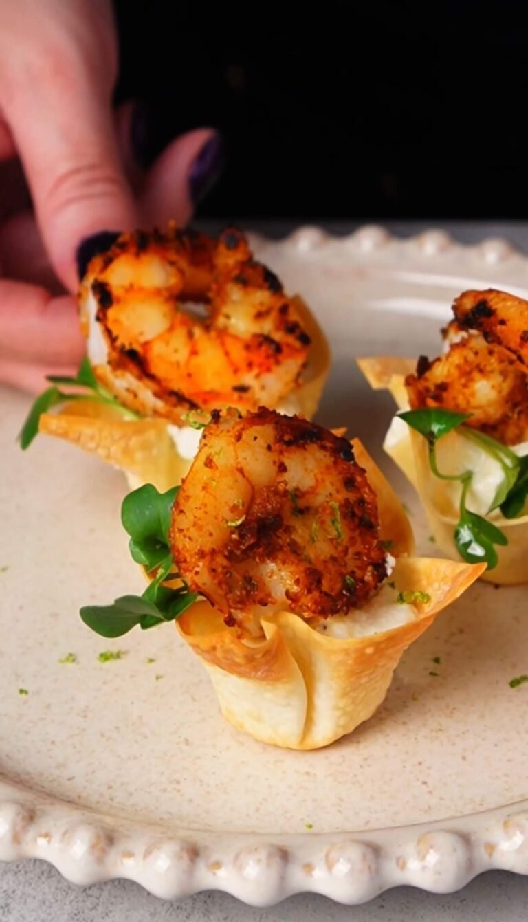 Crispy shrimp wonton cup filled with lime sour cream and topped with Cajun-spiced shrimp and microgreens, served as an elegant appetizer