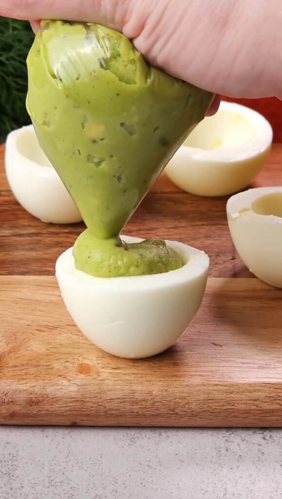 Creamy avocado yolk mixture being piped into a halved hard-boiled egg