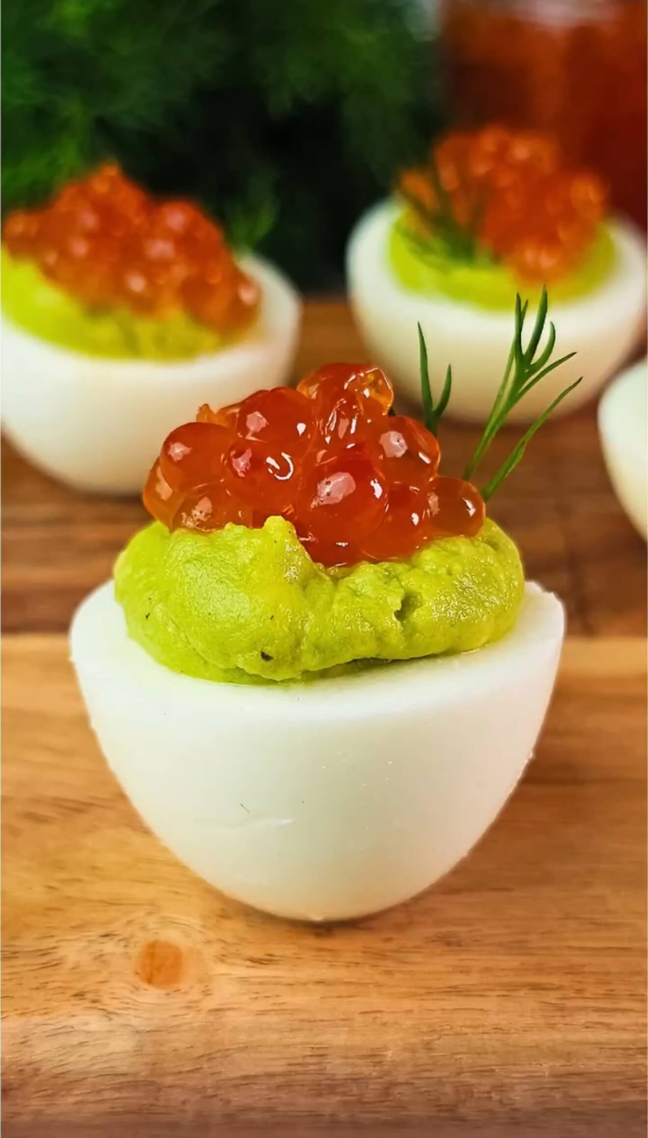 Close-up of an avocado deviled egg topped with red caviar and fresh dill on a wooden board