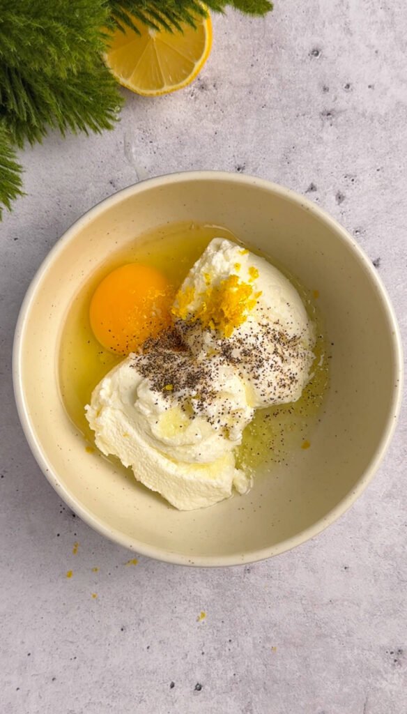 Whole-milk ricotta with egg, lemon zest, olive oil, salt, and black pepper in a bowl before mixing for baked ricotta