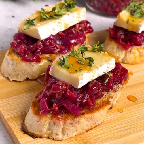 Brie and raspberry crostini arranged on a wooden board with caramelized onion compote and fresh thyme garnish