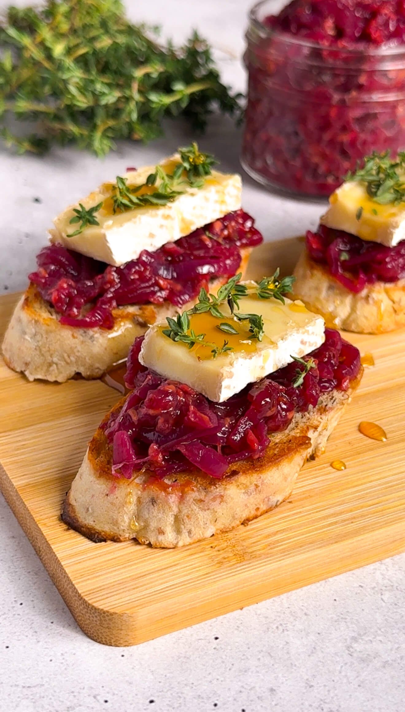 Brie and raspberry crostini arranged on a wooden board with caramelized onion compote and fresh thyme garnish