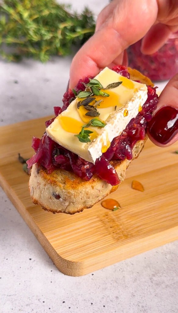 Brie and raspberry crostini topped with caramelized onion compote, creamy brie, fresh thyme, and a drizzle of hot honey on toasted baguette