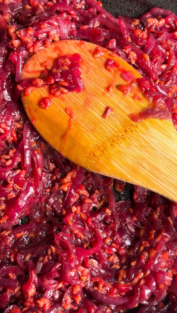 Jammy raspberry caramelized onion compote cooking in a skillet, glossy and thickened for crostini topping