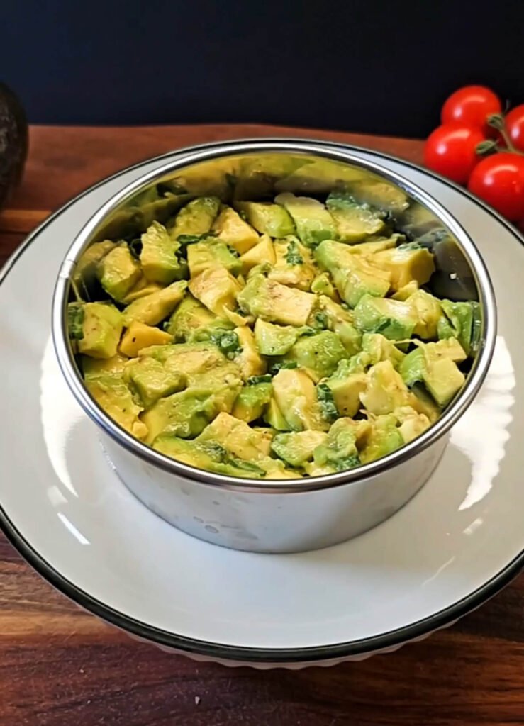 Cubes of avocado tossed with lemon juice and pepper layered on top of cucumber inside a round metal mold