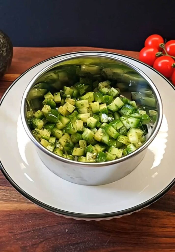 Cubed Persian cucumber mixed with dill and olive oil pressed into a metal ring mold to form the base of a layered salad