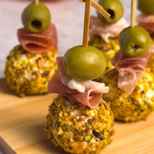 Goat cheese and prosciutto bonbons rolled in pistachios and skewered with Castelvetrano olives on a wooden board