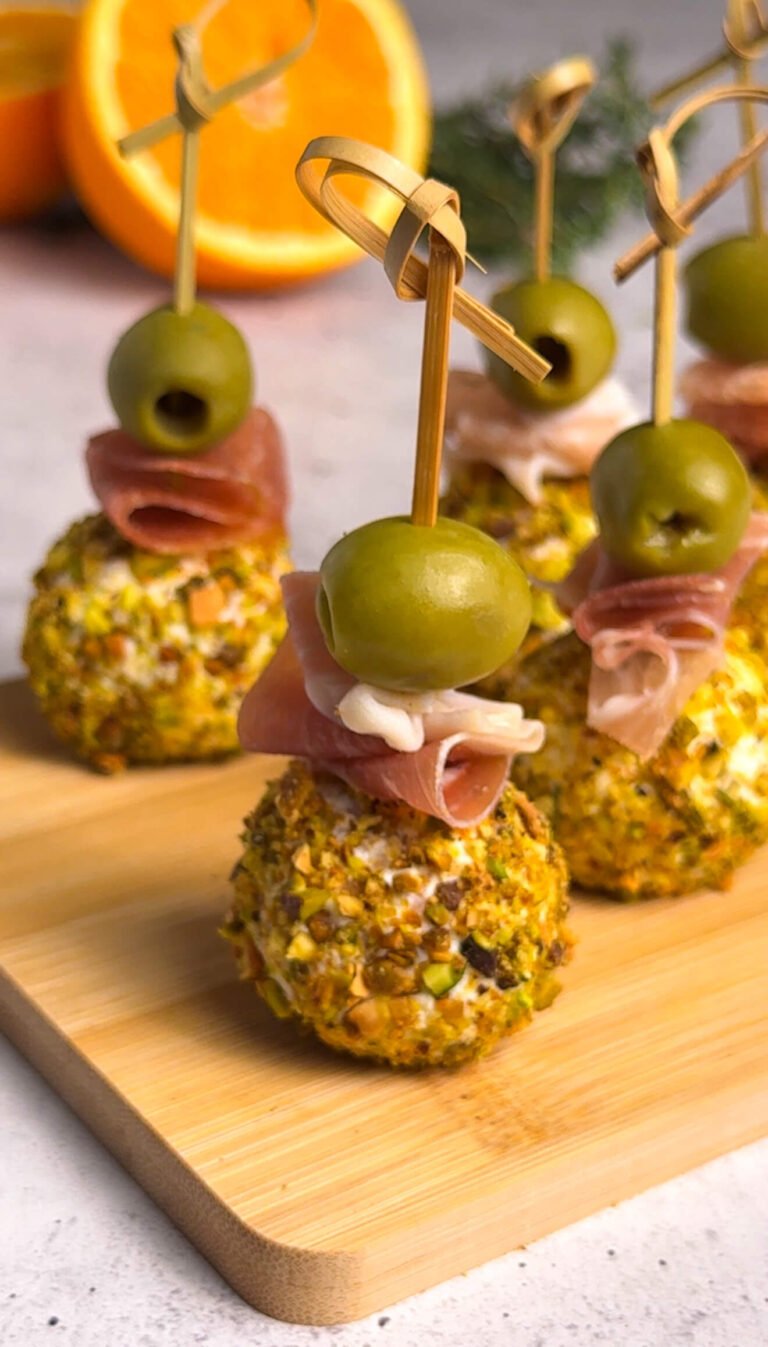 Goat cheese and prosciutto bonbons rolled in pistachios and skewered with Castelvetrano olives on a wooden board