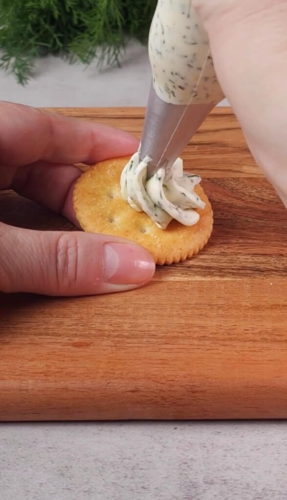 Piping lemon dill whipped cream cheese onto a cracker for an easy smoked salmon appetizer