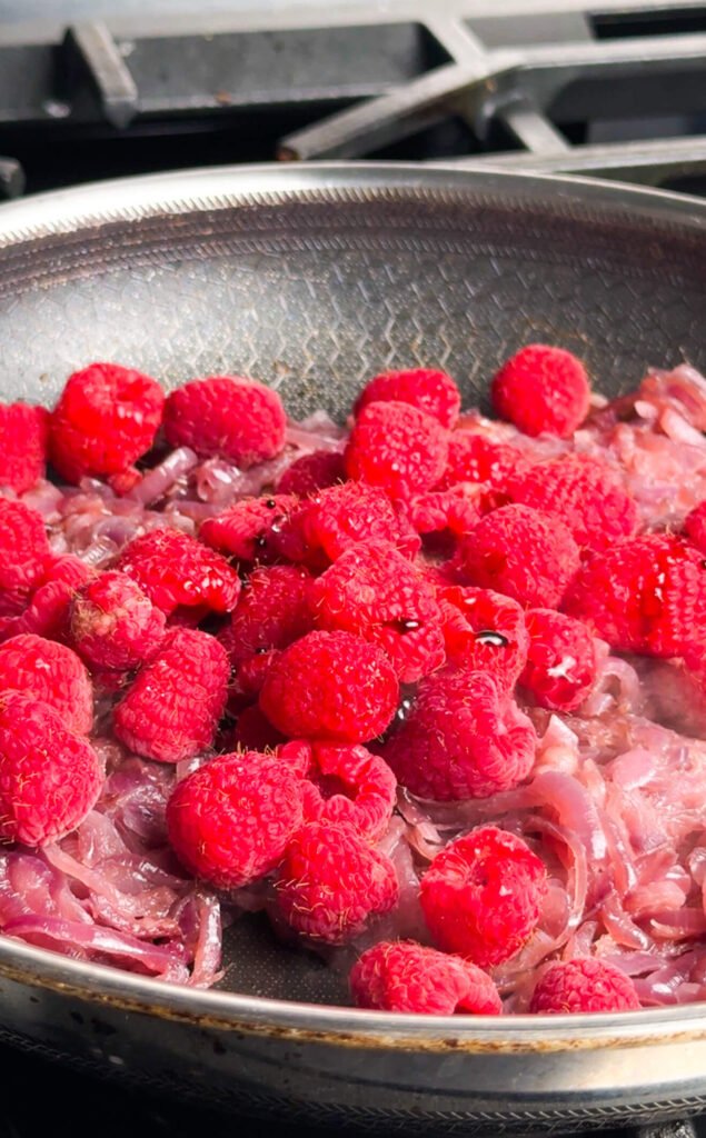 Fresh raspberries added to slowly caramelized red onions in a skillet for raspberry onion compote