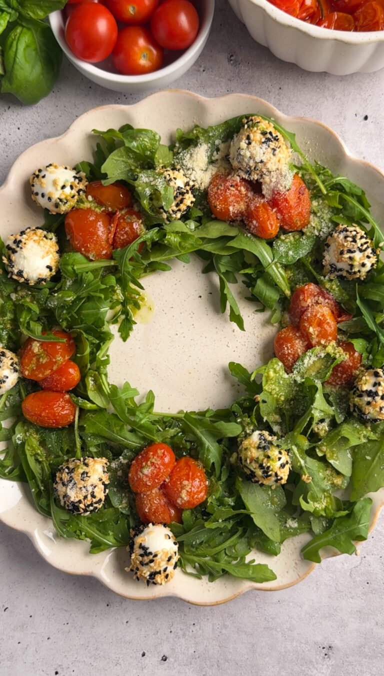 A fully assembled Sesame Mozzarella Balls Wreath on a scalloped platter, topped with roasted cherry tomatoes, sesame-coated mozzarella balls, arugula, and Parmesan.