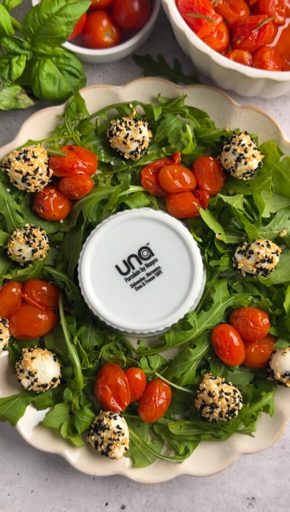 Partially assembled Sesame Mozzarella Balls Wreath with roasted tomatoes and sesame-coated mozzarella balls arranged evenly around the arugula.