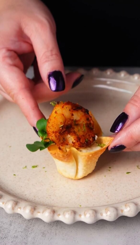 Crispy shrimp wonton cup filled with lime sour cream and topped with Cajun-spiced shrimp and microgreens, served as an elegant appetizer