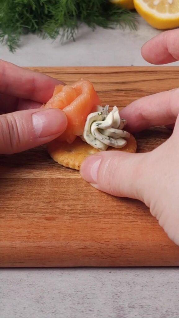 Topping a cream cheese cracker with smoked salmon to make an elegant no-cook appetizer