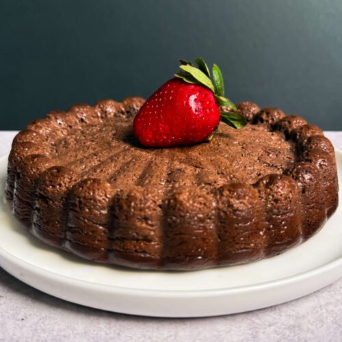 Whole baked chocolate ricotta dessert on a white plate with a fresh strawberry, low-carb and crustless chocolate cheesecake style