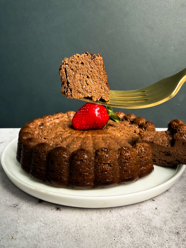 Slice of baked chocolate ricotta dessert lifted on a gold fork, showing dense, cheesecake-like texture, with a strawberry on top