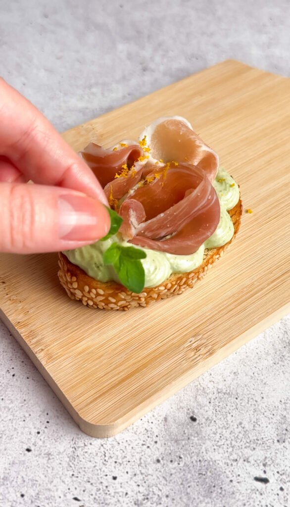Adding fresh basil to crostini with whipped ricotta and prosciutto