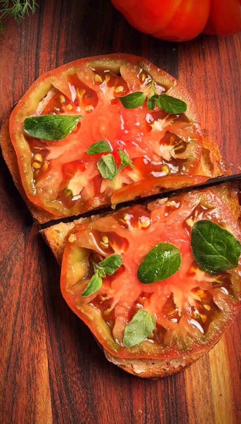 Heirloom tomato toast with anchovy butter, olive oil, and fresh herbs on a wooden board