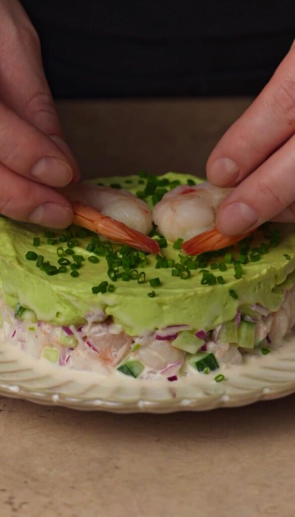 Garnishing shrimp and avocado stack with whole shrimp and fresh chives