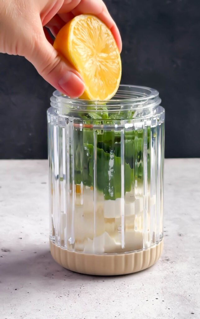 Fresh lemon juice being added to basil whipped ricotta in a food processor