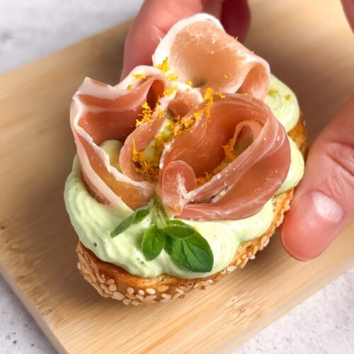 Crostini with whipped ricotta and prosciutto topped with lemon zest and basil