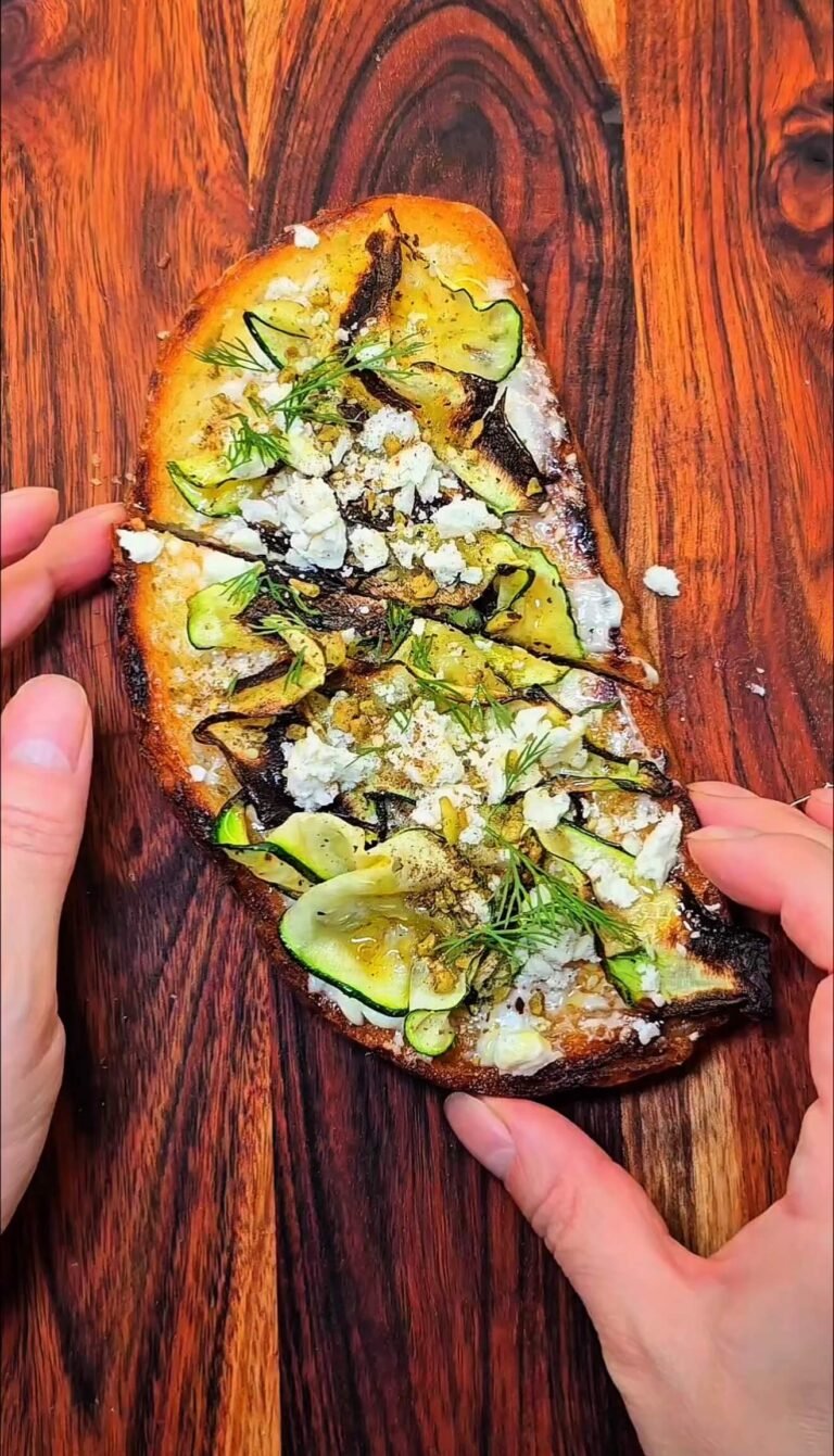 Savory zucchini toast on sourdough topped with broiled zucchini ribbons, crumbled feta, fresh dill, and olive oil on a wooden board