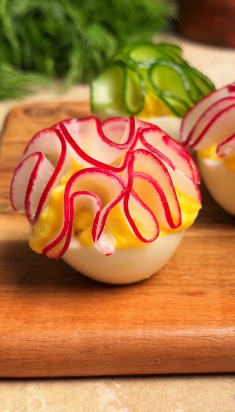 beautiful deviled eggs topped with cucumber and radish flower petals on wooden board