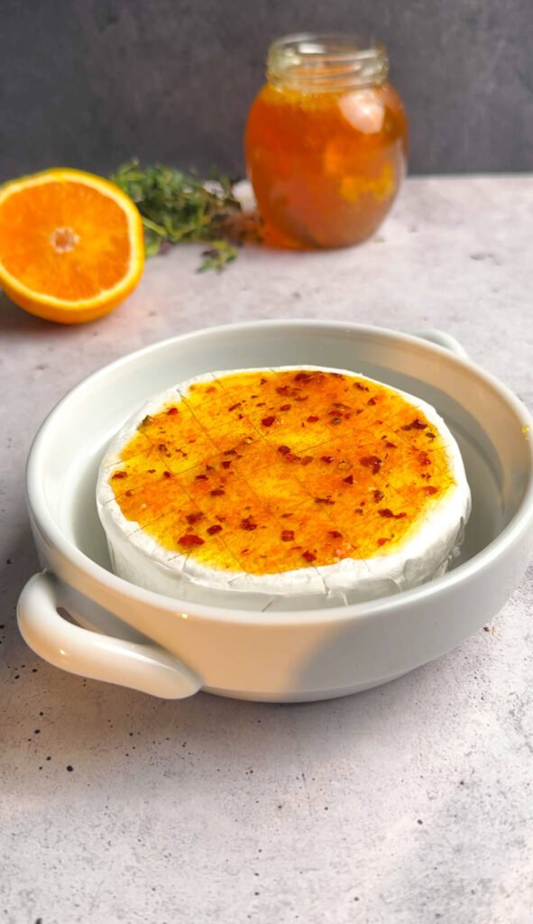 Brie wheel brushed with orange honey glaze and red pepper flakes before baking.