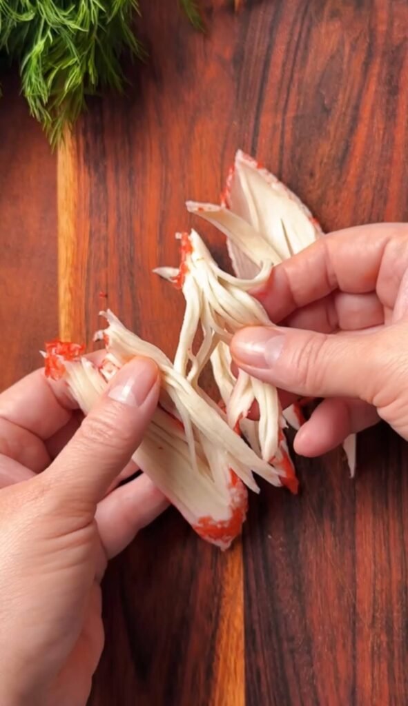 Hands pulling crab sticks into thin strings for chili crisp crab and egg toast