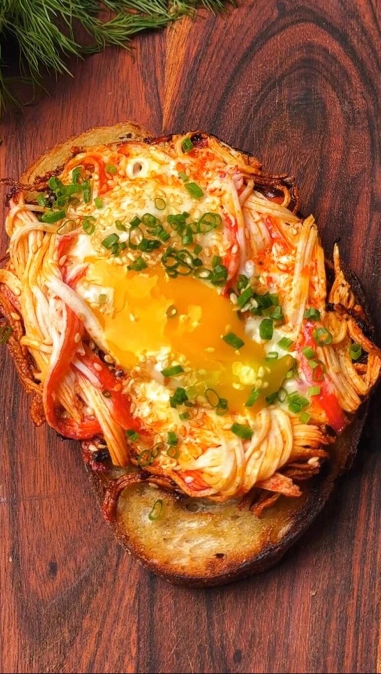 Chili crisp crab and egg toast with pulled crab sticks, jammy egg yolk, sesame seeds, and chives on crispy sourdough