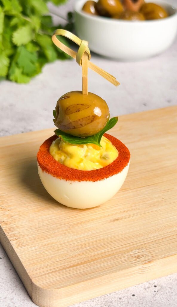 Dirty martini deviled egg garnished with green olive and parsley leaf on bamboo skewer