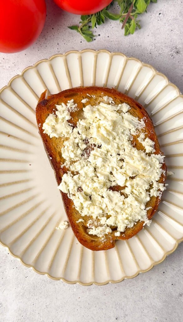 Sourdough toast spread with creamy block feta cheese before adding roasted tomatoes