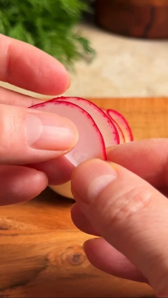 hands folding thin radish slice to create flower petals for deviled eggs