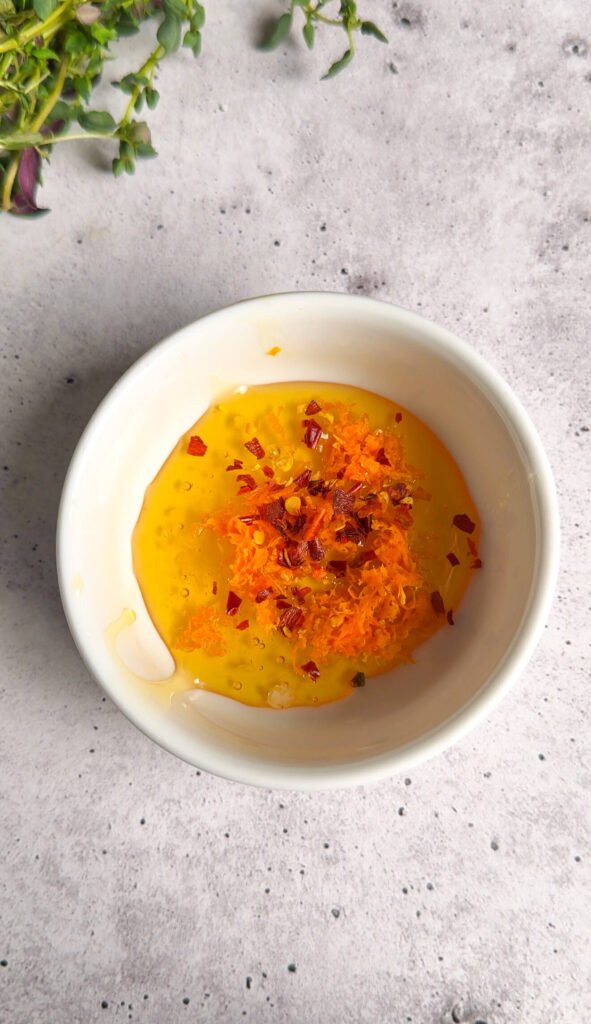 Ingredients for honey glaze including honey, orange zest, and chili flakes in preparation bowl.