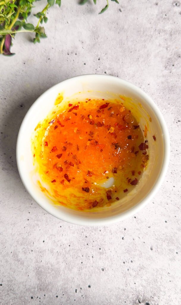 Orange honey glaze mixture with citrus zest and red pepper flakes in a small bowl.