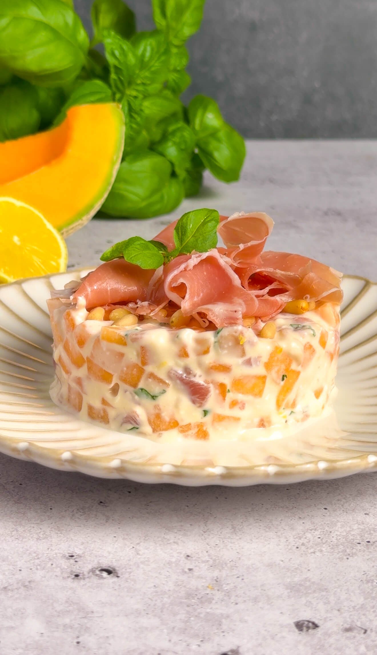 Melon prosciutto tartare with mascarpone cream shaped in a ring mold and topped with silky prosciutto and fresh basil