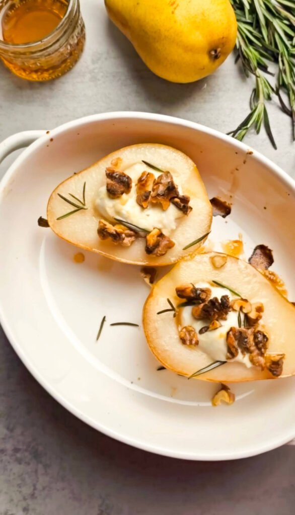 Close-up of baked pear halves with melted goat cheese, honey drizzle, walnuts, and fresh rosemary