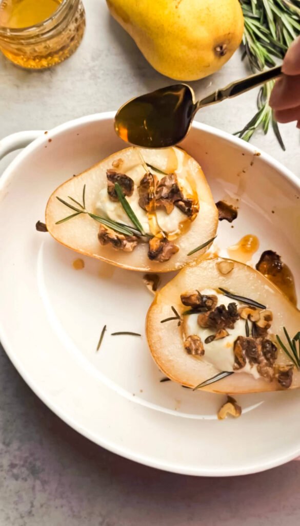 Honey being drizzled over baked pear with goat cheese, walnuts, and rosemary