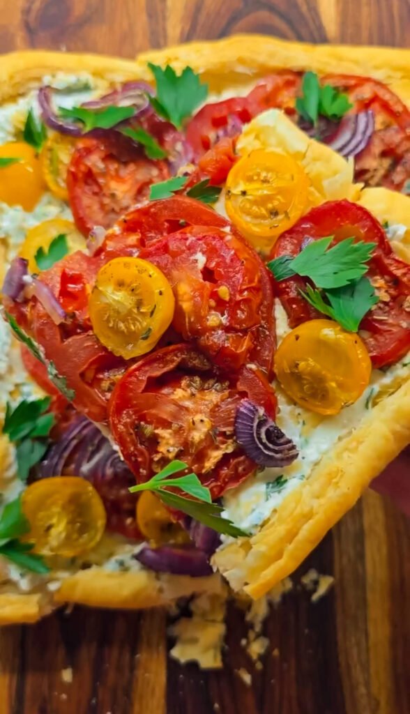 Slice of roasted tomato tart showing creamy cheese layer, jammy roasted tomatoes, and golden puff pastry crust